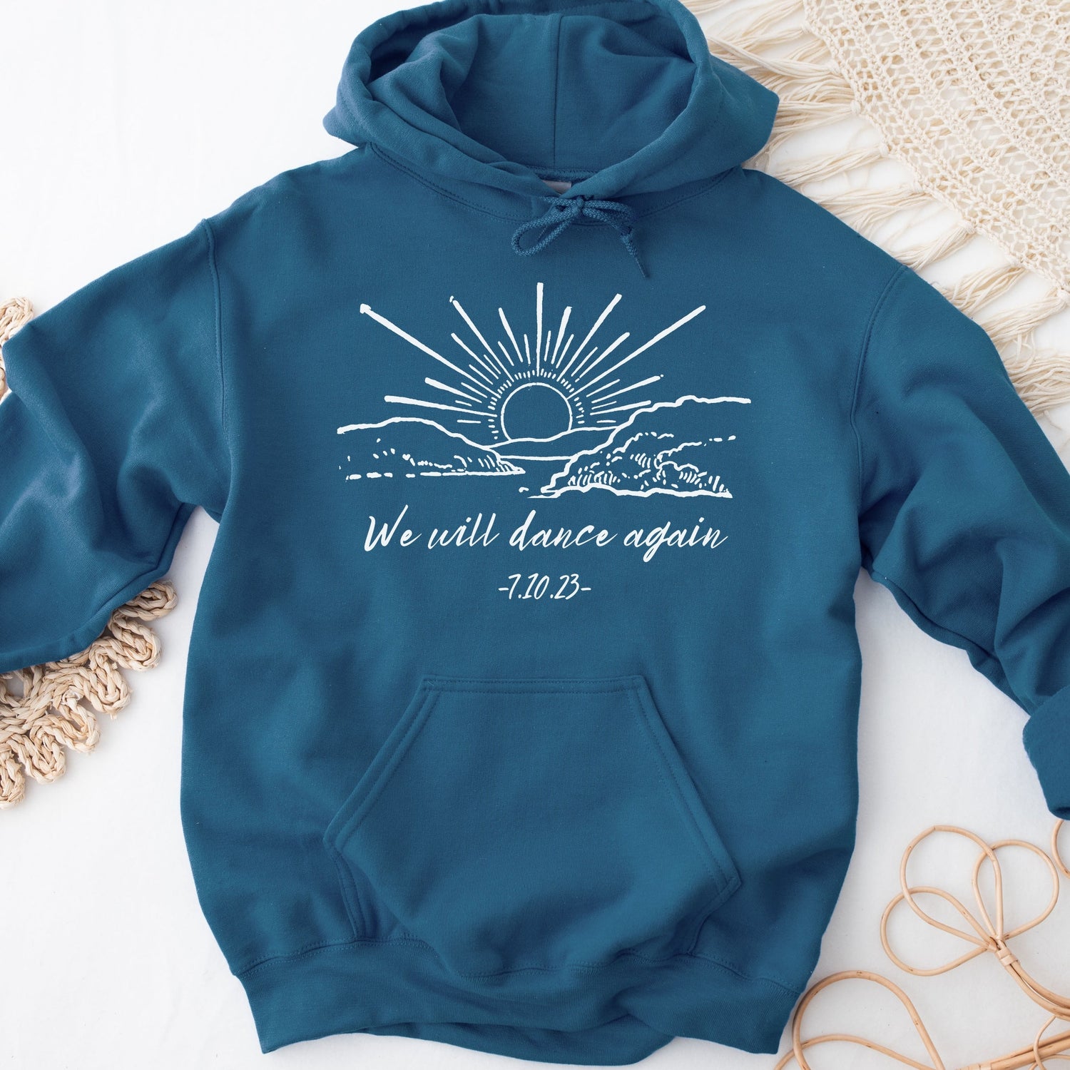 blue hoodie with the phrase "we will dance again 7.10.23" with an illustration of a sunrise 