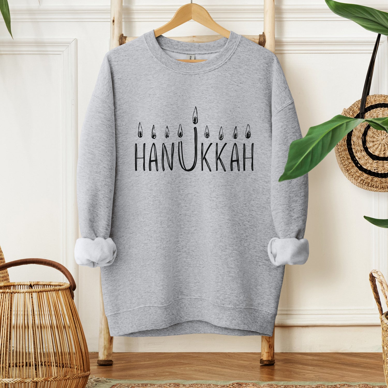 dark heather sweatshirt with a simple illustration of a hanukkah menorah and a quote from Rabbi Schneur Zalman of Liadi "A little bit of light disples a lot of darkness"