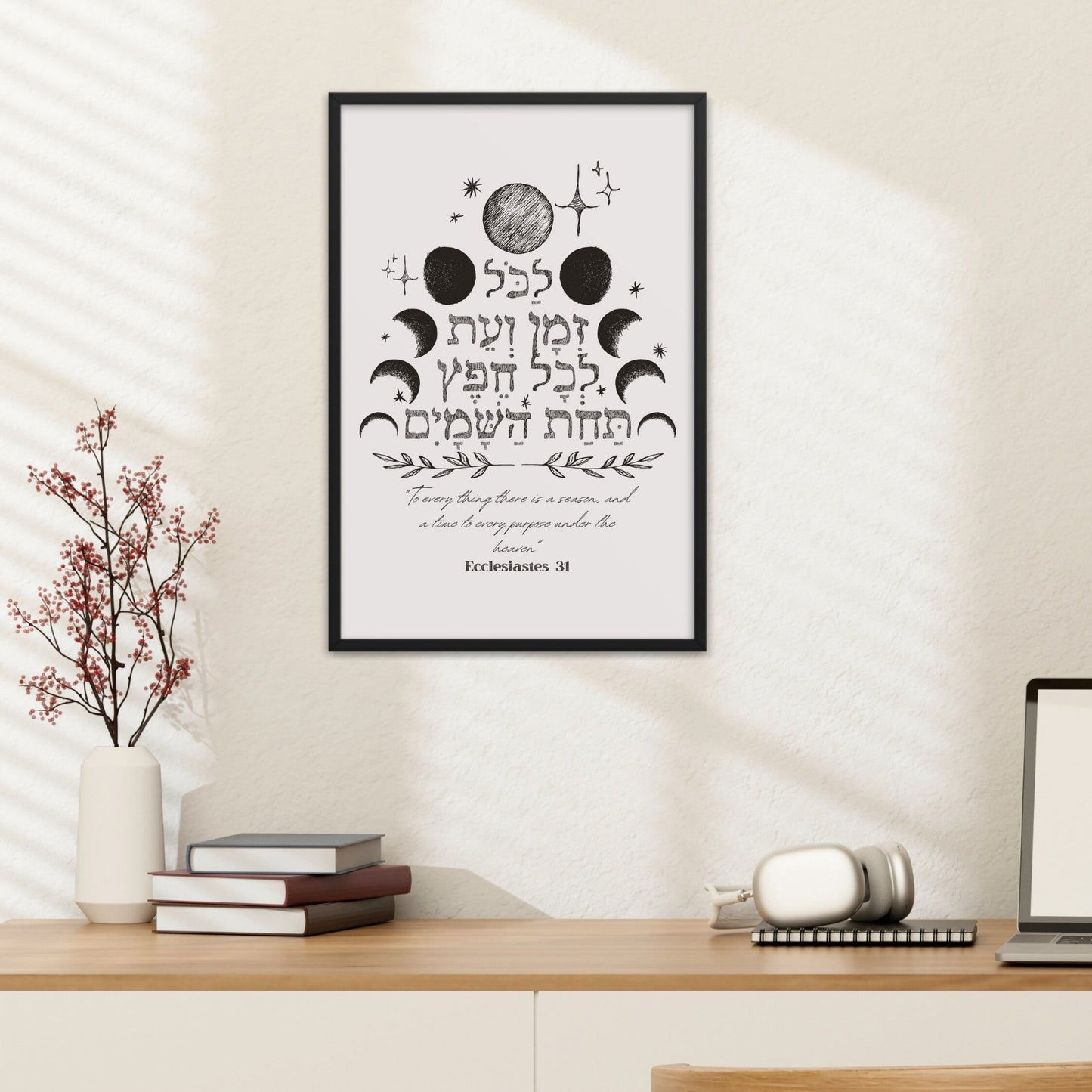 Framed wall art with the verse from Ecclesiastes 3:1 in Hebrew, featuring celestial designs, hung above a desk with a lamp and books.