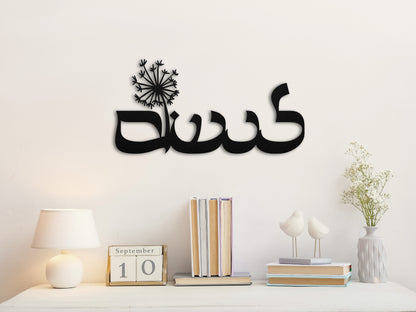 "לנשום" metal sign with a dandelion, positioned above a desk with a stack of books and a small vase of flowers.