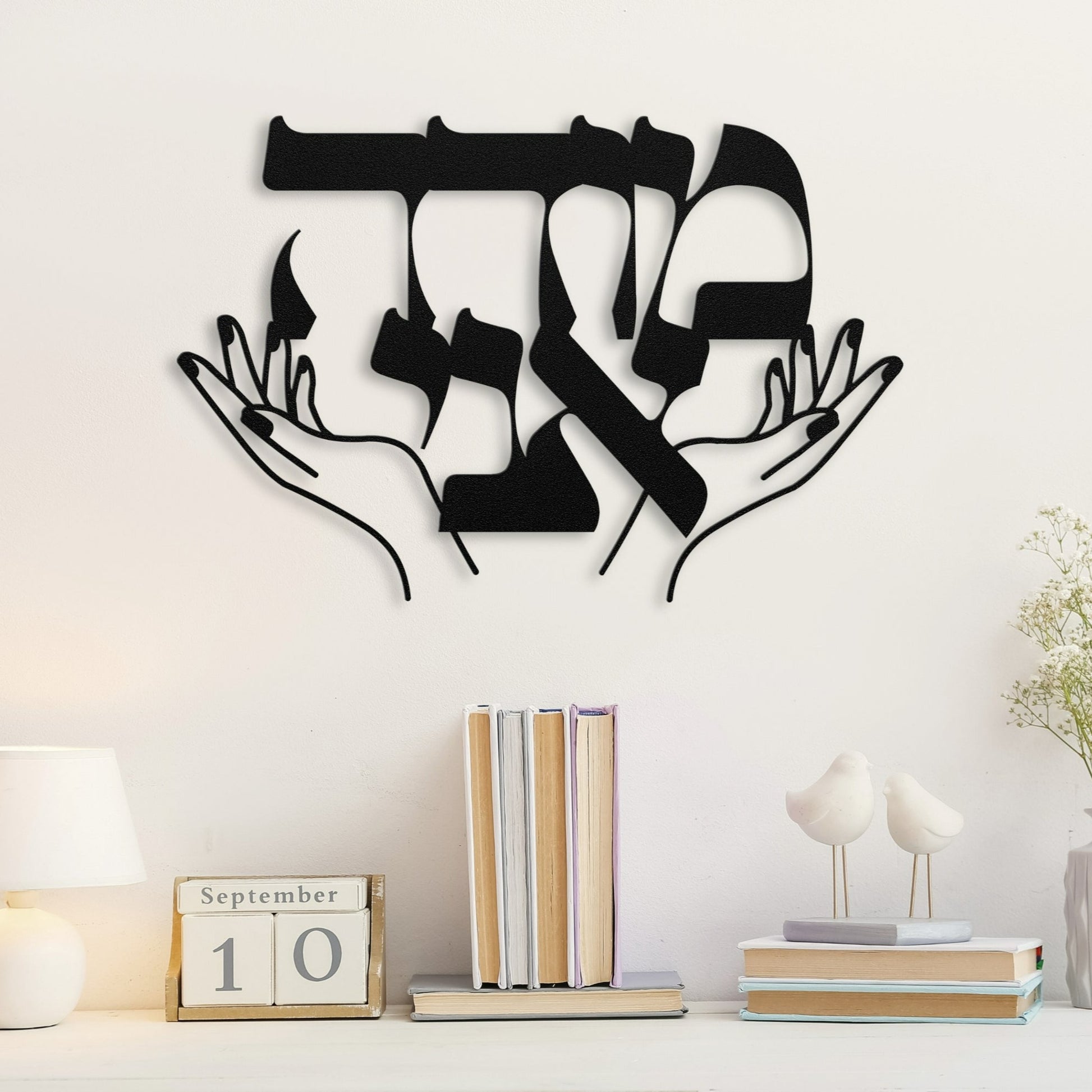 Metal wall art featuring the Hebrew phrase "מודה אני" (Modeh Ani), with an elegant design of hands raised in prayer or blessing. Placed above a desk with books and a table lamp, the piece adds a spiritual and artistic touch to the room.