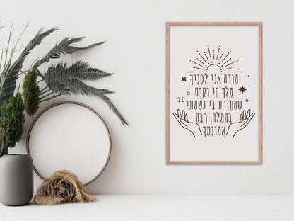 Framed wall art with the Hebrew phrase 'מודה אני' (Modeh Ani), featuring hands and sunburst design, displayed next to a vase and dried botanical decor.