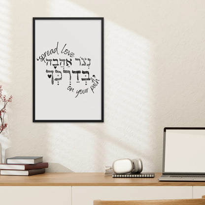 Framed wall art with the Hebrew phrase 'נצור אהבה בדרכך' (Spread love on your path), featuring a minimalist design, hung above a desk with a lamp and books.