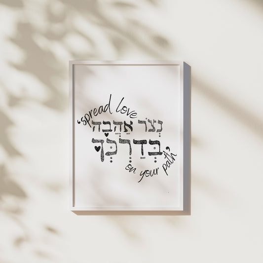 Framed wall art with the Hebrew phrase 'נצור אהבה בדרכך' (Spread love on your path), featuring a minimalist design, hung on a wall with light shadows.