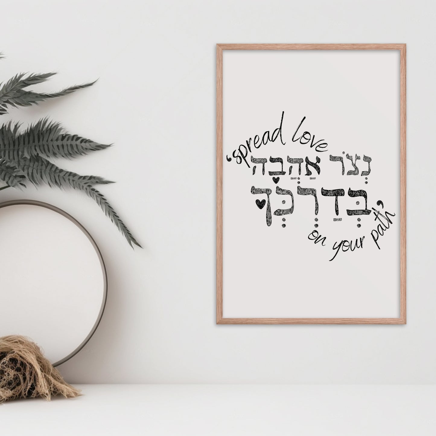 Framed wall art with the Hebrew phrase 'נצור אהבה בדרכך' (Spread love on your path), featuring a minimalist design, displayed next to a vase and dried botanical decor.