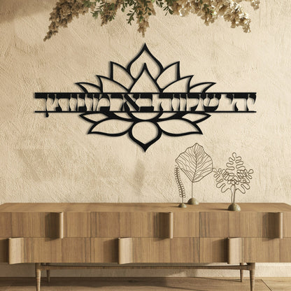 A stylish metal wall art piece featuring the Hebrew phrase "יהי שלווה בארמונותיך" (May there be peace within your walls) with a decorative lotus flower design. The art is displayed against a textured wall above a wooden cabinet, creating a harmonious and serene ambiance.