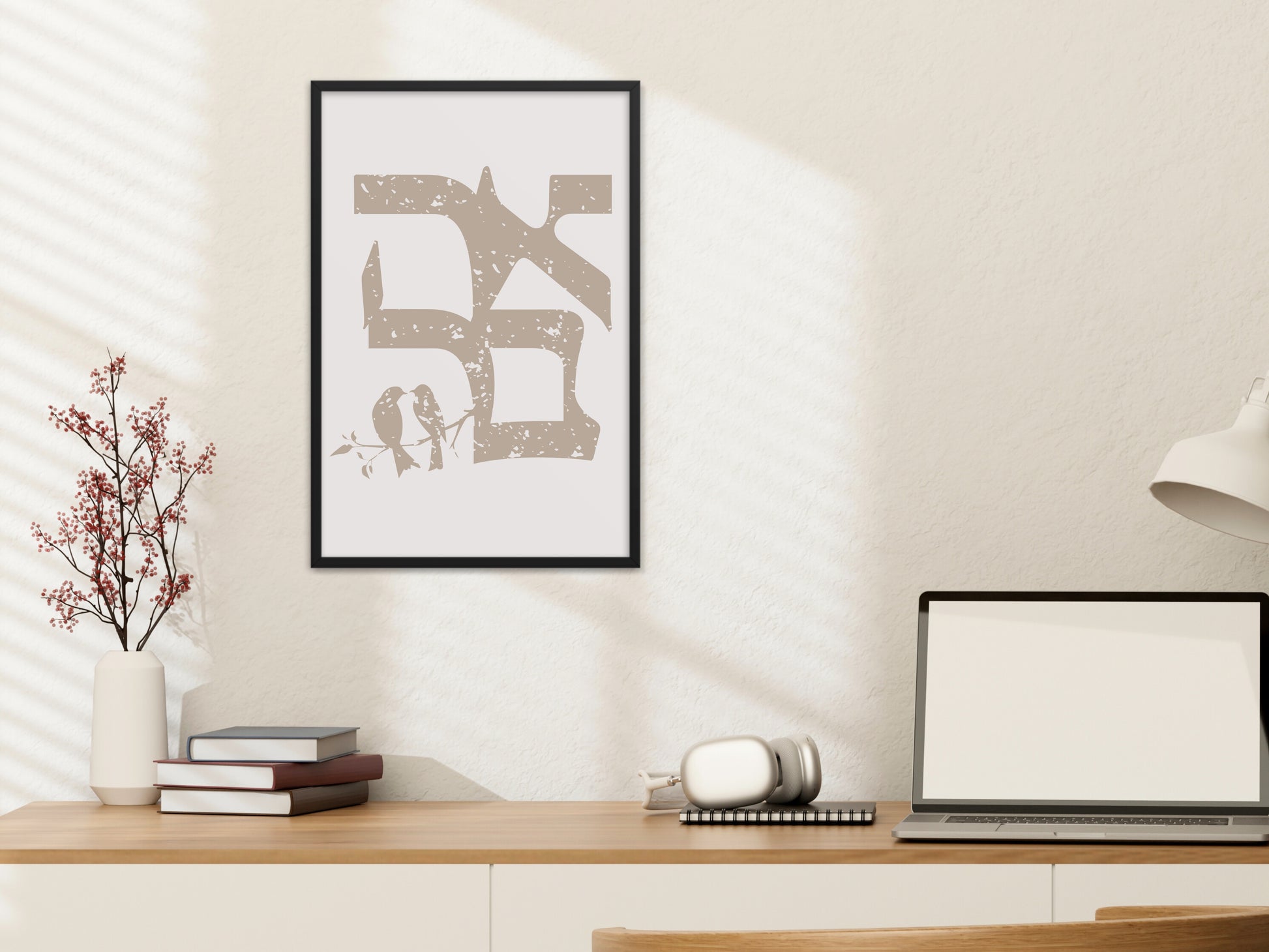 Framed wall art of the Hebrew word 'אהבה' (Love) in a vintage distressed style, with two birds on a branch, hung above a desk with books and a laptop.