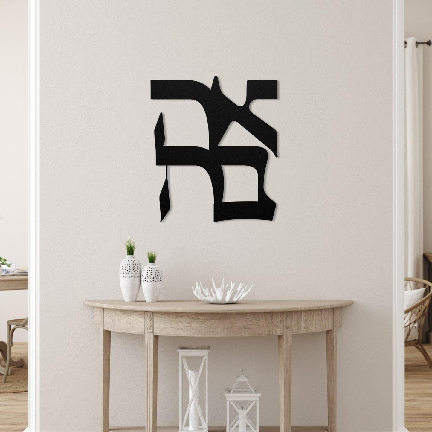 Decorative metal wall art featuring the Hebrew word 'אהבה' (love) mounted on a white wall in a modern, minimalist living room with a wooden console table and white ceramic decor pieces.