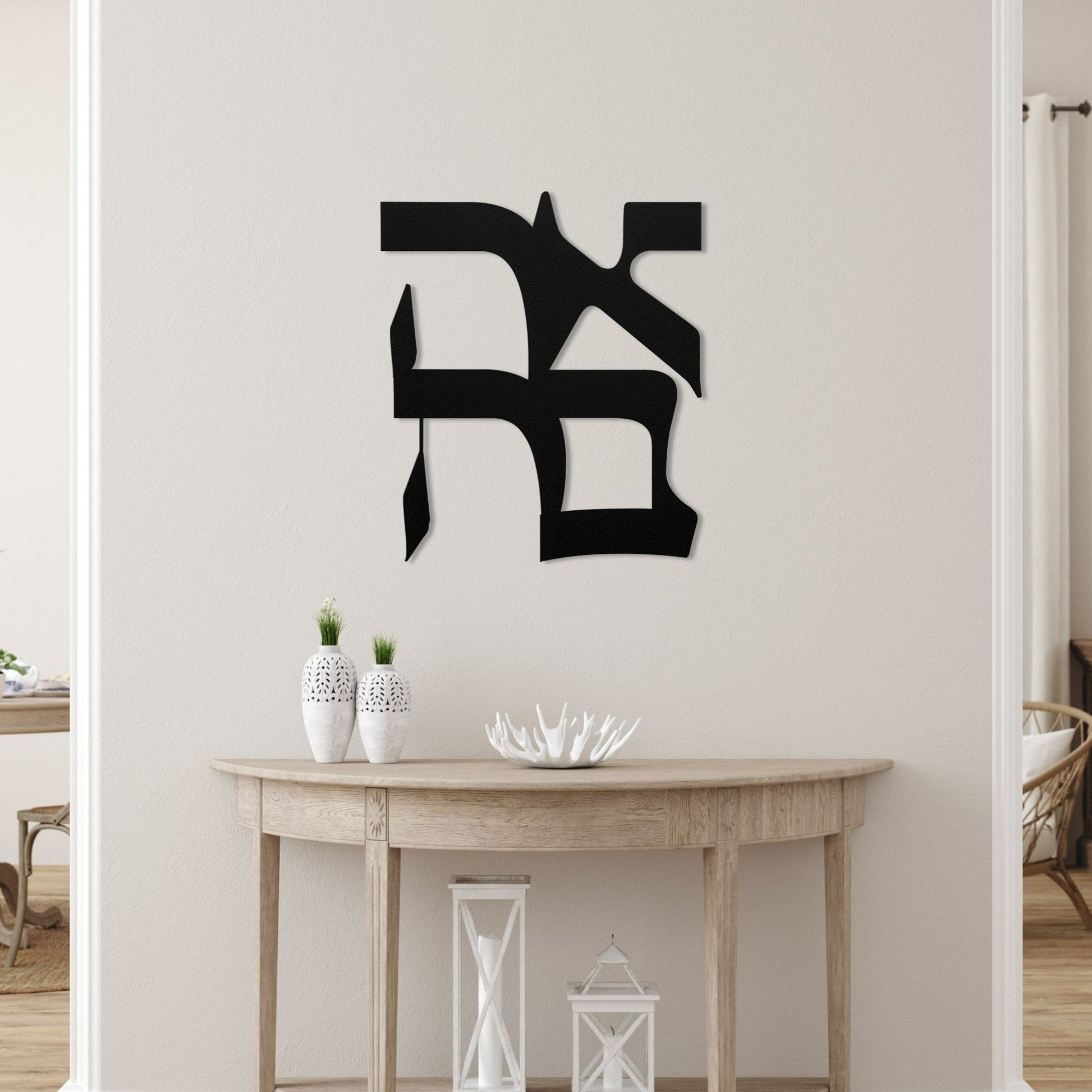 Decorative metal wall art featuring the Hebrew word 'אהבה' (love) mounted on a white wall in a modern, minimalist living room with a wooden console table and white ceramic decor pieces.