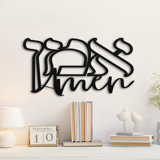 beautifully designed 'אמן' (Amen) Hebrew metal wall art mounted on a white wall. The wall art is positioned above a wooden console table adorned with books, a small lamp, and decorative white bird figurines.