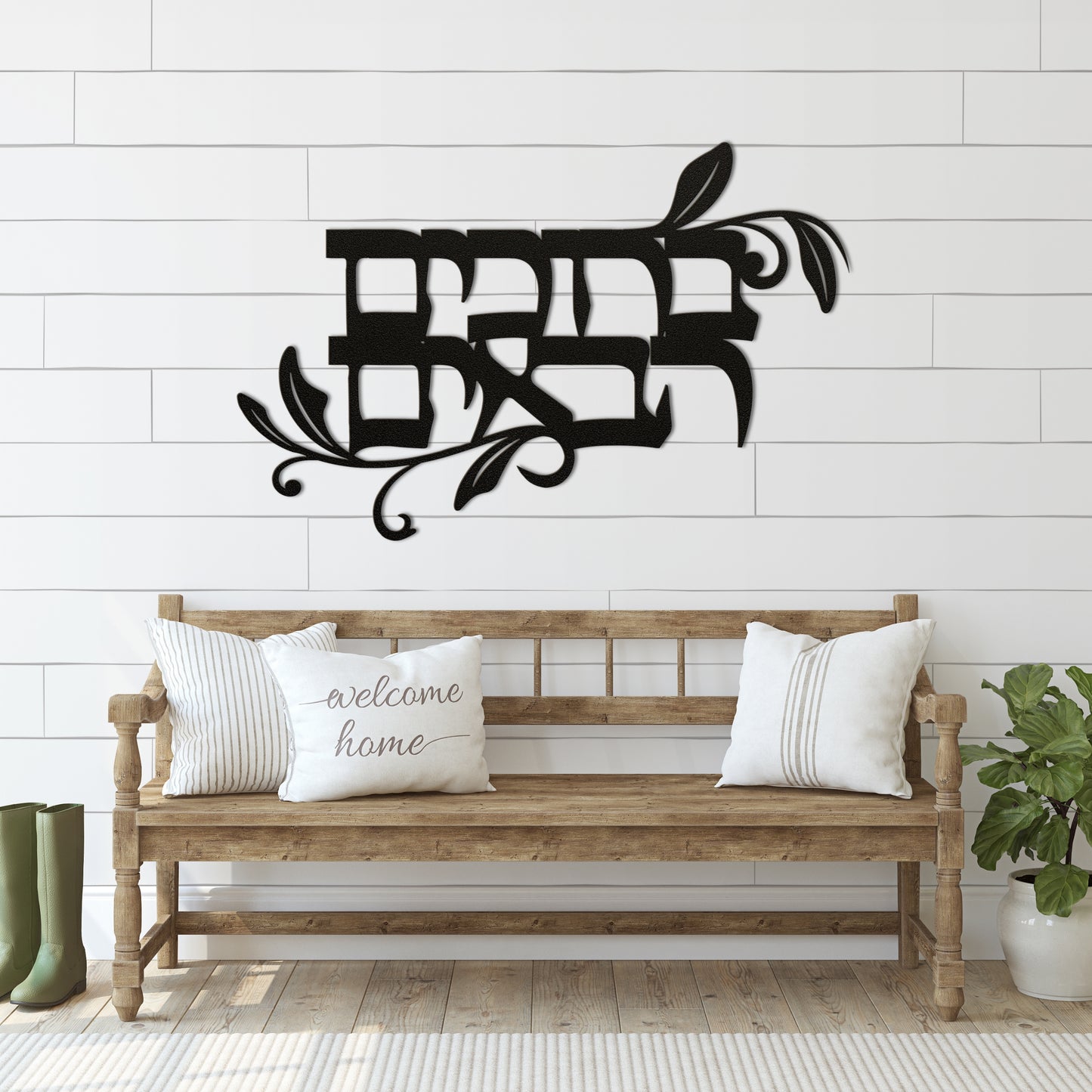 Powder-coated die-cut metal sign with the Hebrew phrase 'ברוכים הבאים' (Welcome), hung above a bench with welcome-themed cushions, set against a shiplap wall.