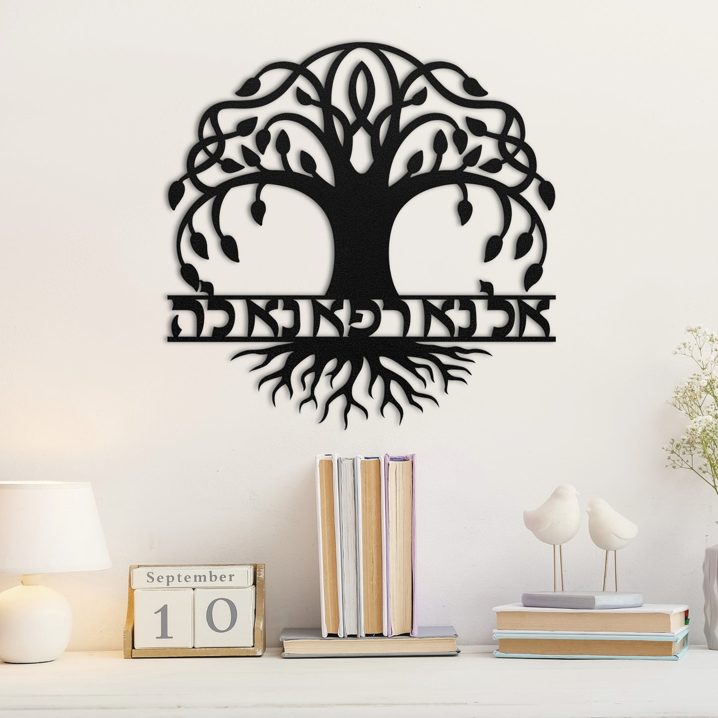 Living room wall with 'אל נא רפא נא לה' (O God, please let us be healed) Tree of Life metal wall art, featuring a large tree with Hebrew text integrated into the design, mounted above a bookshelf with books and decorative items.