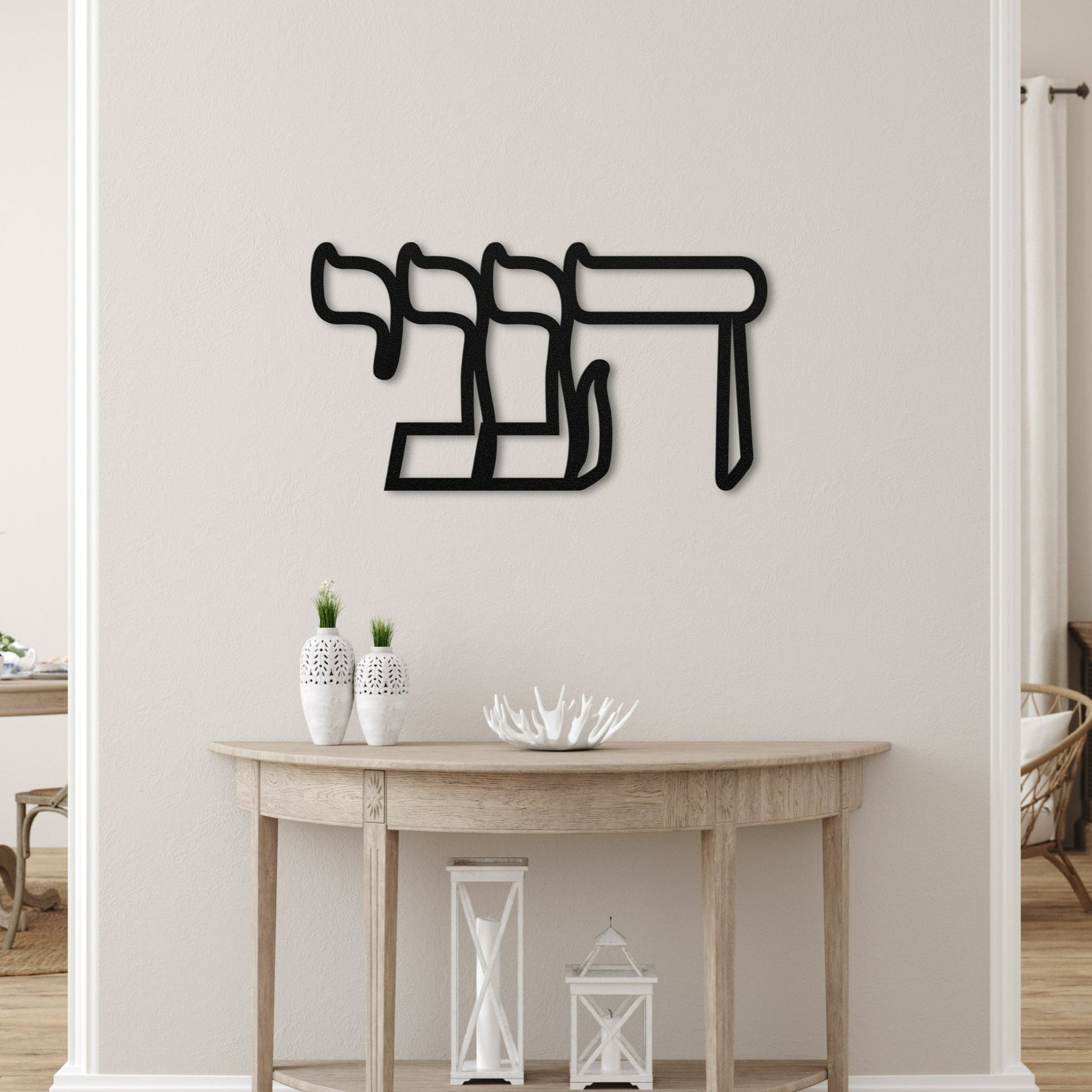 Elegant metal wall art featuring the Hebrew word 'הנני' (here I am), displayed in a serene, modern living space with minimalistic decor and neutral tones.