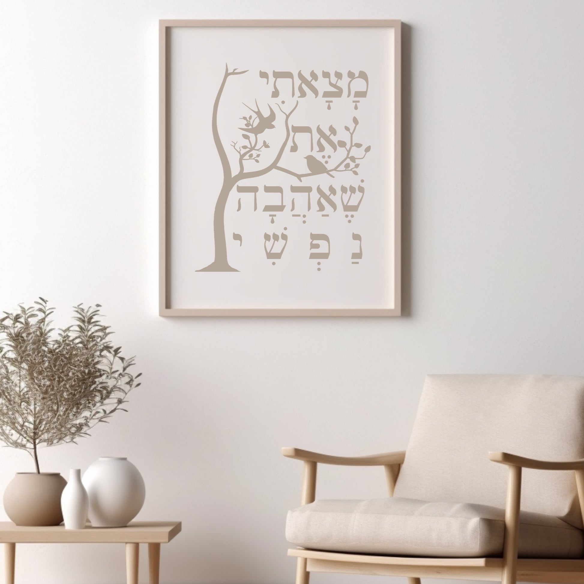 Framed wall art featuring a tree and the Hebrew verse 'מצאתי את שאהבה נפשי' (I have found the one whom my soul loves), displayed above a chair with decorative plants nearby.