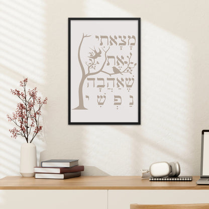 Framed wall art with a tree and the Hebrew verse 'מצאתי את שאהבה נפשי' (I have found the one whom my soul loves), hung above a desk with a lamp, books, and decorative branches.