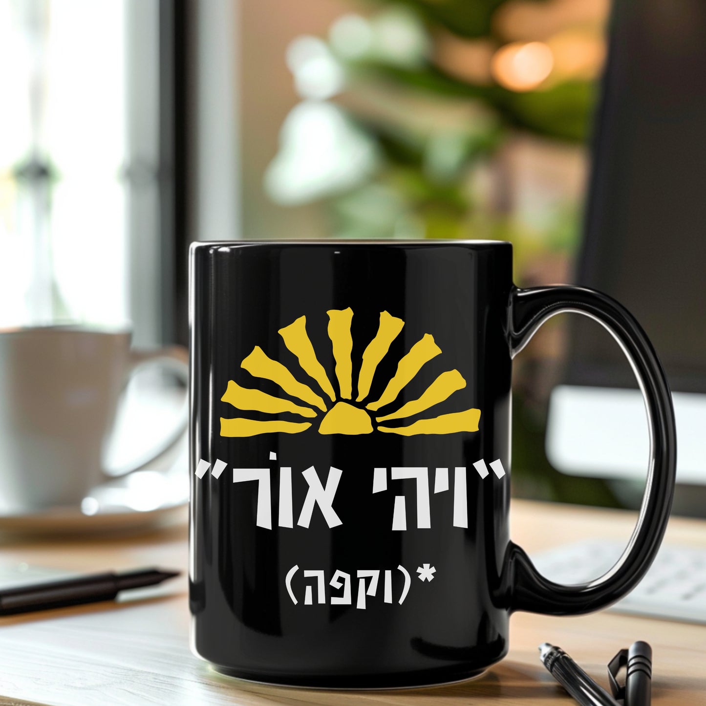 A black ceramic mug featuring the biblical quote "ויהי אור" (Let There Be Light) with the humorous addition "וקפה" (and coffee) and a sun illustration, sitting on a desk with a blurred background of a coffee cup and a notepad.