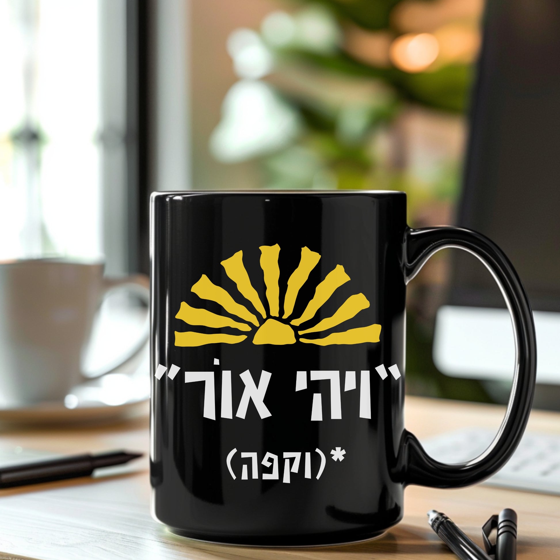 A black ceramic mug featuring the biblical quote "ויהי אור" (Let There Be Light) with the humorous addition "וקפה" (and coffee) and a sun illustration, sitting on a desk with a blurred background of a coffee cup and a notepad.