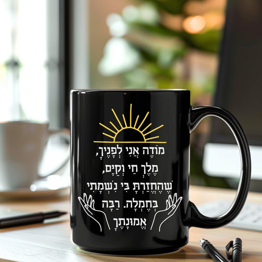 modeh ani prayer in hebrew black coffee mug on a working desk with a desktop and pencils.