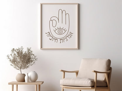 Framed wall art with the Hebrew phrase 'אנרגיות חיוביות' (Positive Energy) and a hamsa hand design, displayed above a chair with decorative plants nearby.