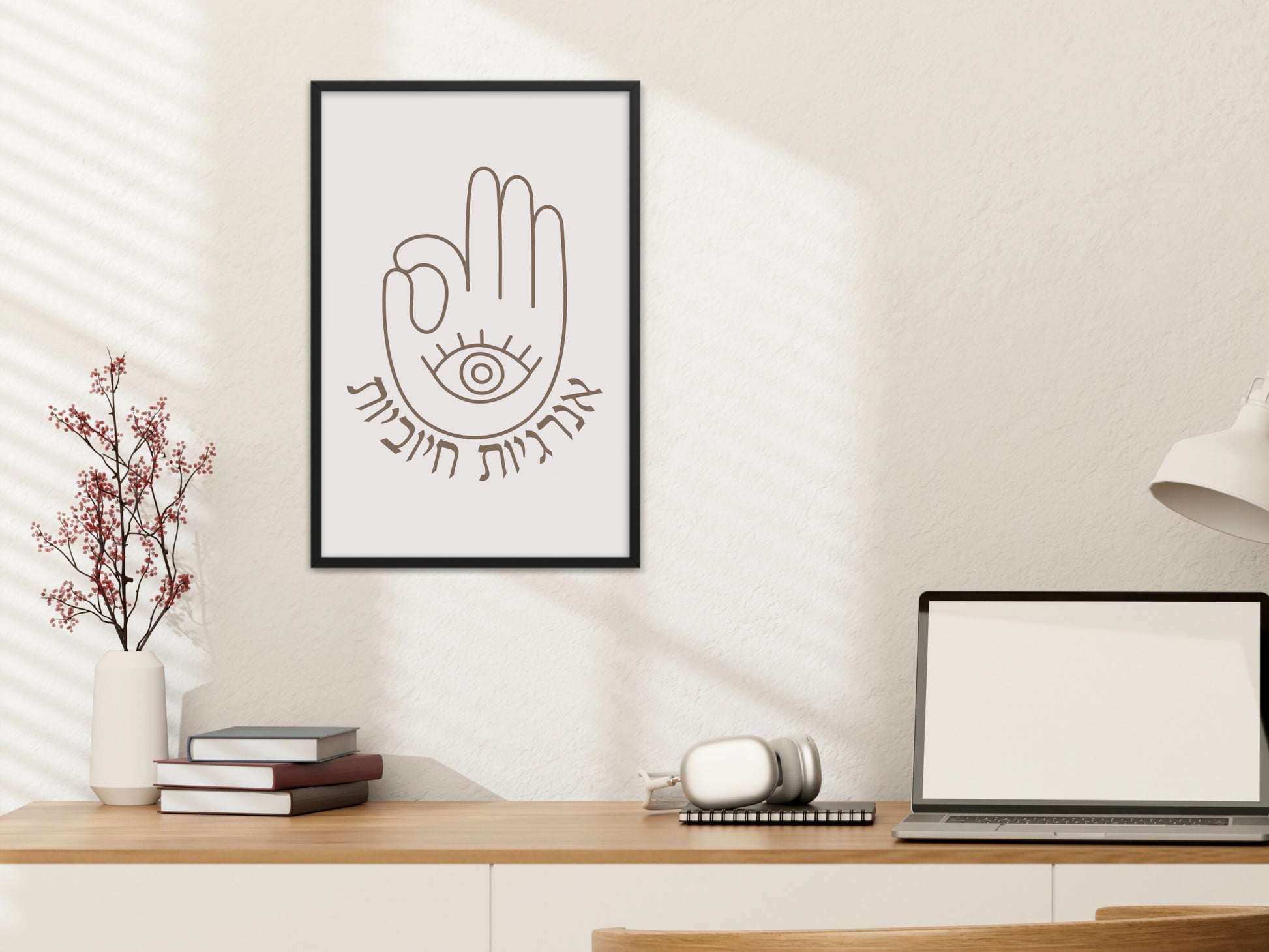 Framed wall art with the Hebrew phrase 'אנרגיות חיוביות' (Positive Energy) and a hamsa hand design, hung above a desk with a lamp and books.