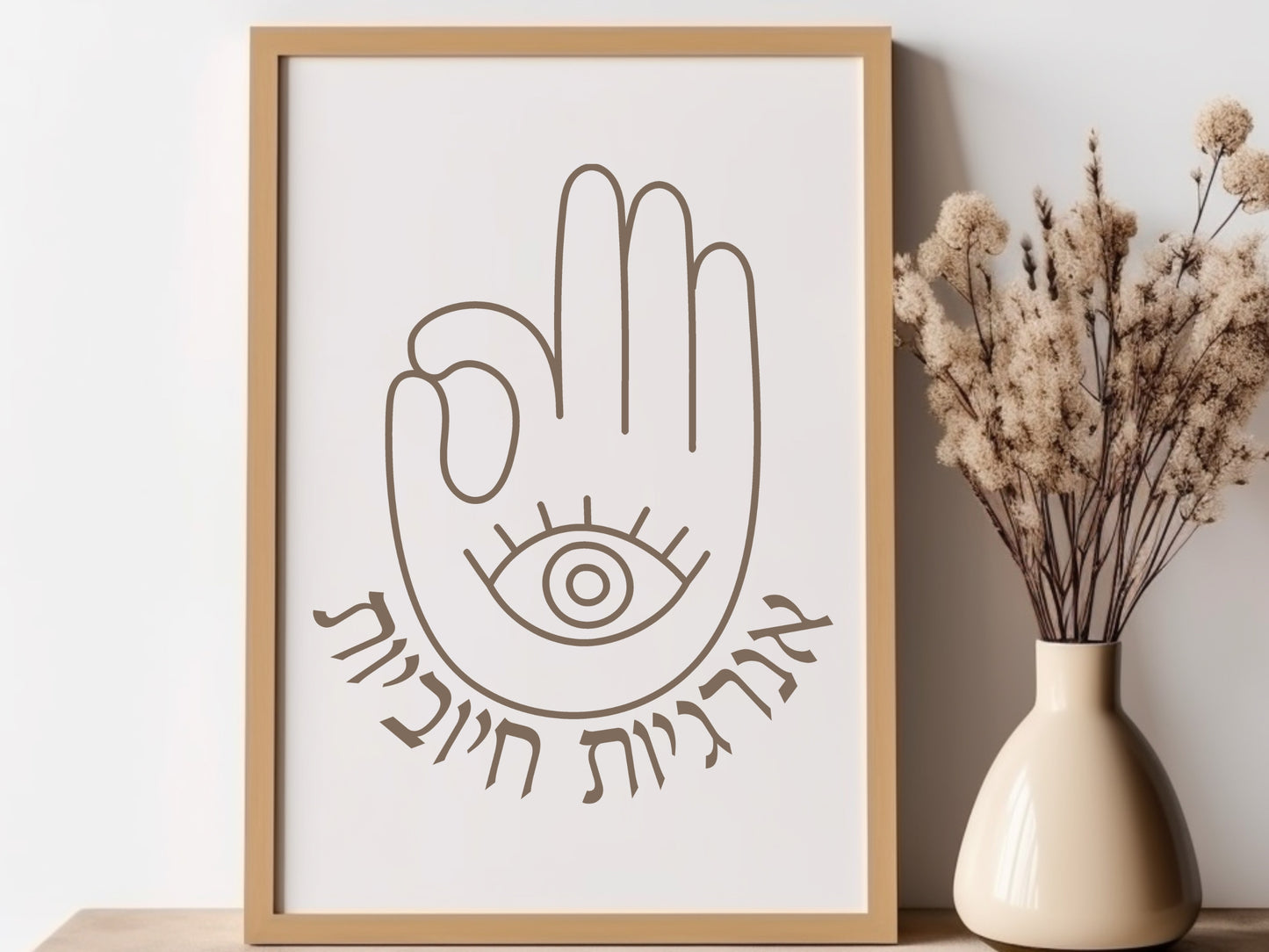 Framed wall art with the Hebrew phrase 'אנרגיות חיוביות' (Positive Energy) and a hamsa hand design, placed next to a vase with dried flowers.