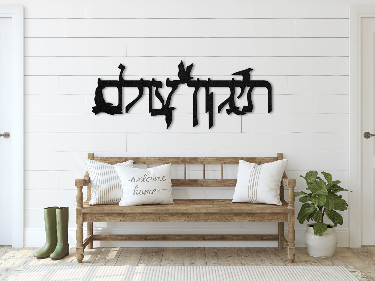 Metal sign "תיקון עולם" with flying doves on a white shiplap wall above a wooden bench with striped pillows and a welcoming atmosphere.